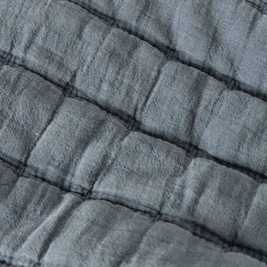 A close-up of a quilted fabric with a textured, crinkled linen-like surface in a muted slate blue colour.