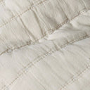 Cose-up of a quilted fabric in a warm off-white or cream colour, showing stitched square panels.