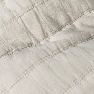 Cose-up of a quilted fabric in a warm off-white or cream colour, showing stitched square panels.