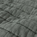 Close-up of a quilted bedspread in a muted green colour.