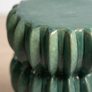 Close-up of a glossy ceramic pedestal  table in a muted jade glaze, showing the fluted pedestal base and rounded top surface.