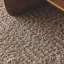 close-up of a textured area rug with floral and vine pattern in warm taupe, brown, and cream tones.