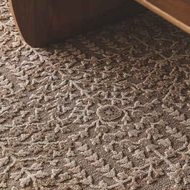 close-up of a textured area rug with floral and vine pattern in warm taupe, brown, and cream tones.