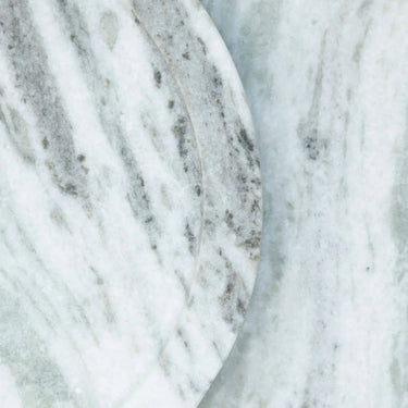 A close-up of a polished white marble surface with soft gray veining and a curved edge visible.