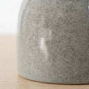 Close-up of a speckled grey ceramic side table base resting on a light wood surface against a white background.
