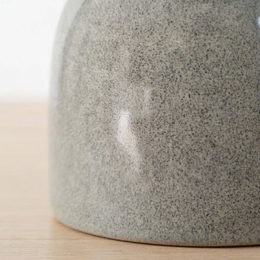 Close-up of a speckled grey ceramic side table base resting on a light wood surface against a white background.