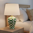 The Green Swirl Lamp on a wooden bedside table providing a warm, soft glow in a cozy bedroom setting.