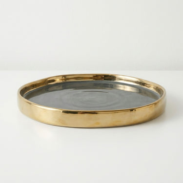A round tray with a polished gold-toned  rim and a dark gray interior.