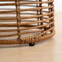 Close-up of a woven rattan side table   natural brown wicker slats photographed on a light wood floor