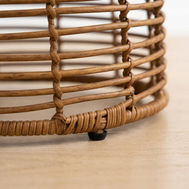 Close-up of a woven rattan side table   natural brown wicker slats photographed on a light wood floor