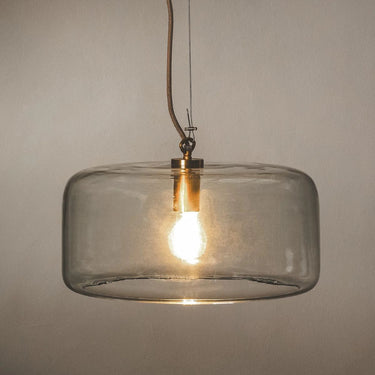 Pendant light with a clear glass shade and a warm glowing bulb inside, suspended by a cord.