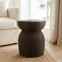 Dark brown rattan living room side table placed on a woven rug in a bright living room next to a cream sofa.