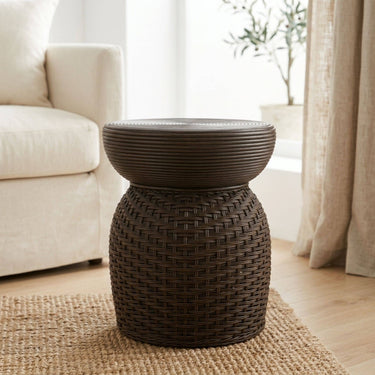 Dark brown rattan living room side table placed on a woven rug in a bright living room next to a cream sofa.