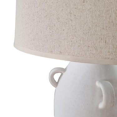 Close-up of a white ceramic lamp with a beige fabric shade on a white background