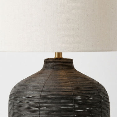 Close-up of a table lamp with a dark woven cane base and a cream linen drum shade.