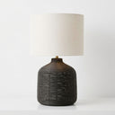 black table lamp with a textured  base and a cylindrical off-white fabric drum shade.