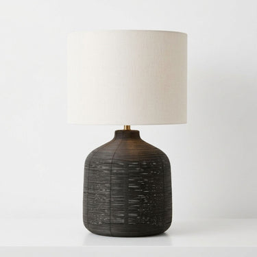 black table lamp with a textured  base and a cylindrical off-white fabric drum shade.