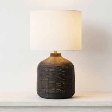 Illuminated Luna black rattan modern lamp featuring a moody, sophisticated look and warm glowing beige fabric shade