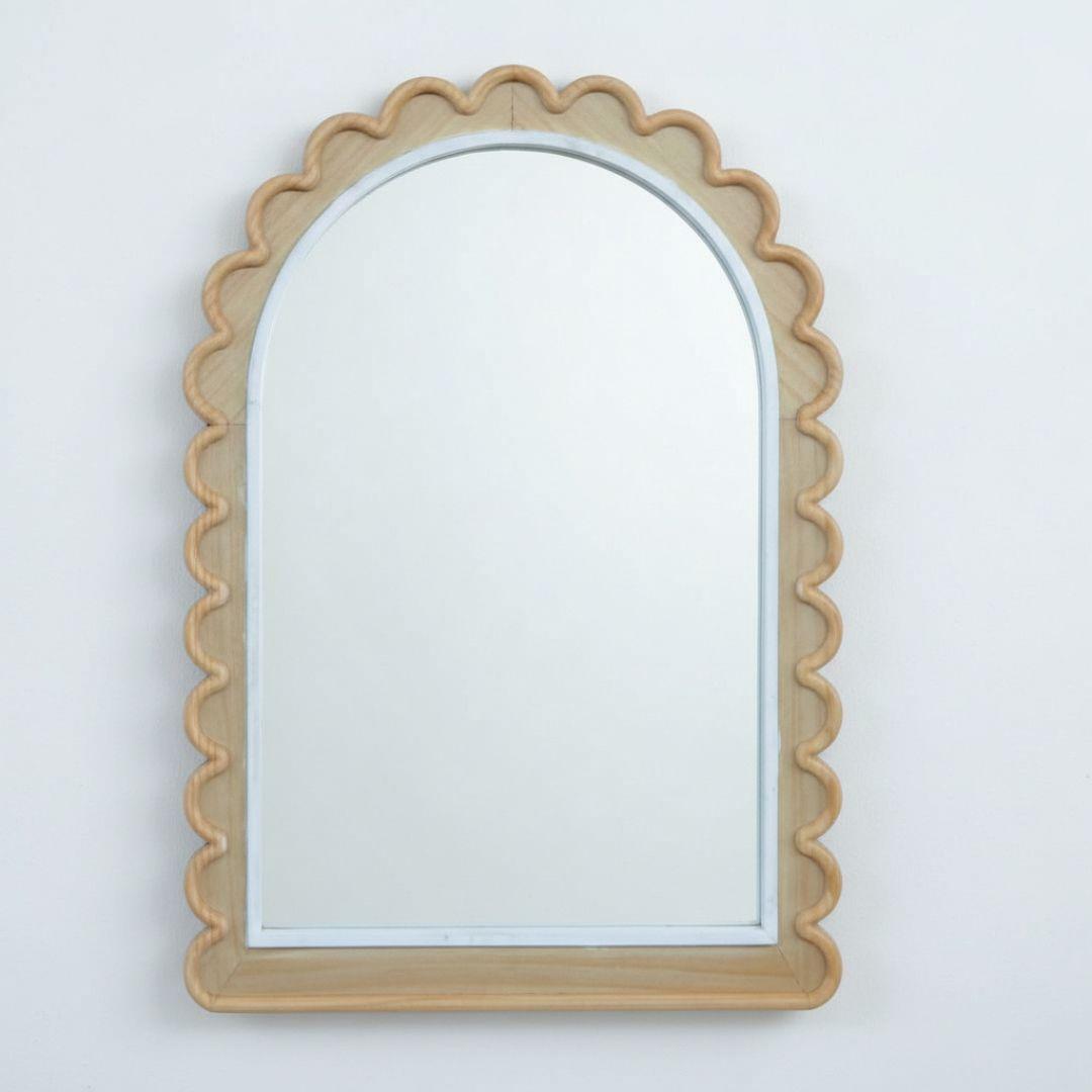 Arched scalloped wood mirror styled on a minimalist wall to add warmth and sculptural interest to a modern room.