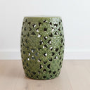 Green ceramic stool with intricate lace-like design on a light wooden floor.