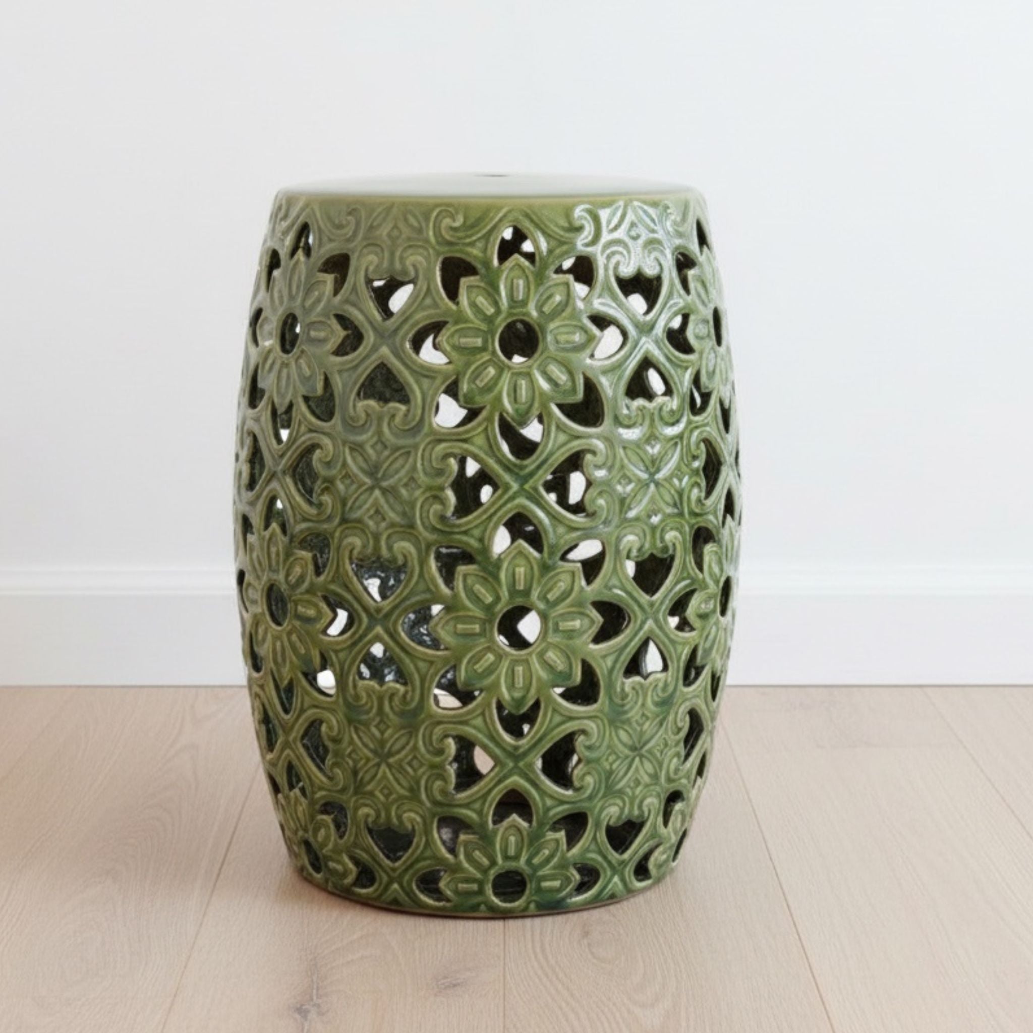 Green ceramic stool with intricate lace-like design on a light wooden floor.