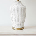 Detailed view of the white-brushed rattan cane weave of the mira lamp sitting on a sleek, polished solid brass base plate