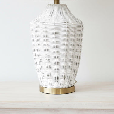 Detailed view of the white-brushed rattan cane weave of the mira lamp sitting on a sleek, polished solid brass base plate