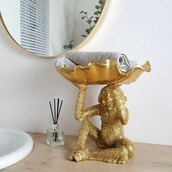 gold monkey shape bowl with petal on head next to a gold framed mirror.