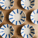 Top-down view of Mykonos flat ceramic bowls with hand-painted cobalt blue radial stripes on a textured cream background.