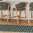 Three upholstered counter stools with olive green fabric seats and backs in kitchen setting with a striped green rug on the floor.