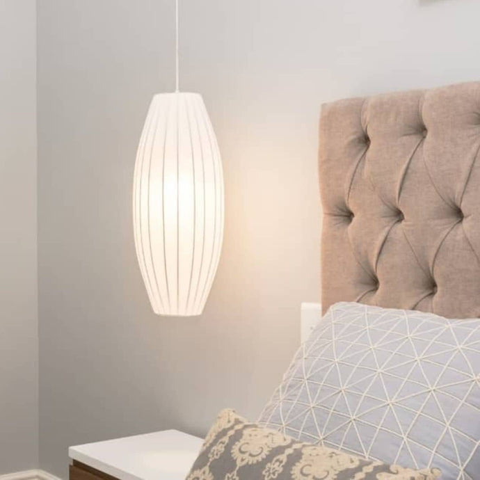 White pendant light hanging above a bed with a tufted headboard and geometric pillow.