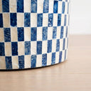 Close-up of a round accent table with a blue and cream checkered pattern, resting on a light wood surface.