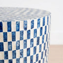 A close-up of a cylindrical table with a blue and pearl checkerboard pattern made from textured rectangular capiz tiles.