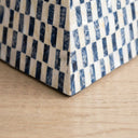 A close-up of a checkered pattern on a side table  with dark blue and off-white tones resting on a light wood surface.