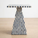 A accent side table with a rectangular top and tapered base, covered in a blue and owhite checkerboard capiz-inlay pattern, set on a light wood floor against a white wall.
