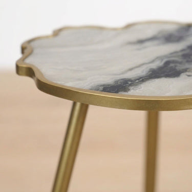 Close-up of a cloud-shaped side table with a white and gray marbled  effect top and a brushed gold metal frame.