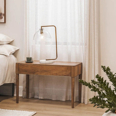 sienna wooden side table with lamp next to a bed in a bedroom setting