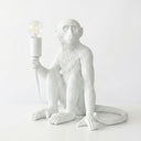 A white monkey-shaped table lamp holding an exposed Edison bulb, set against a clean white background.