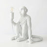 A white monkey-shaped table lamp holding an exposed Edison bulb, set against a clean white background.