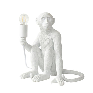 A white monkey-shaped table lamp holding an exposed Edison-style light bulb, shown on a plain white background.