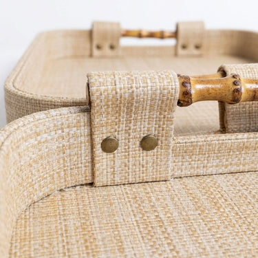 Woven beige tray with a bamboo handle and brass-tone hardware against a white background.