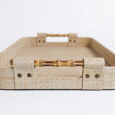 A rectangular woven tray with a natural beige raffia inen-like texture and bamboo-style handles.