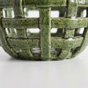 Close-up of a ceramic bowl with a green speckled glaze and a lattice cutout pattern.