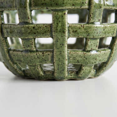 Close-up of a ceramic bowl with a green speckled glaze and a lattice cutout pattern.