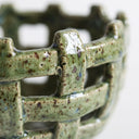 Close-up of a ceramic basketweave bowl with a glossy green glaze and brown speckles.
