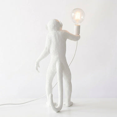 A white monkey-shaped table lamp holding a clear glass bulb, photographed against a clean white background.