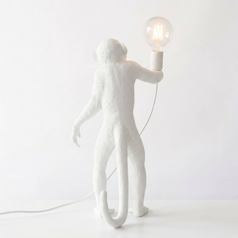 A white monkey-shaped table lamp holding a clear glass bulb, photographed against a clean white background.