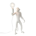 A white monkey figurine lamp holding a clear glass bulb with a warm glowing filament, shown on a plain white background.