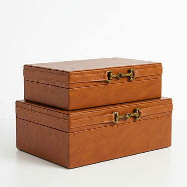 Two stacked rectangular brown faux-leather storage boxes with brass horsebit-style clasps.