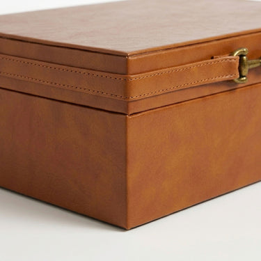 Close-up of a rectangular brown faux-leather storage box with a hinged lid, stitched seam detail, and a brass-tone latch.